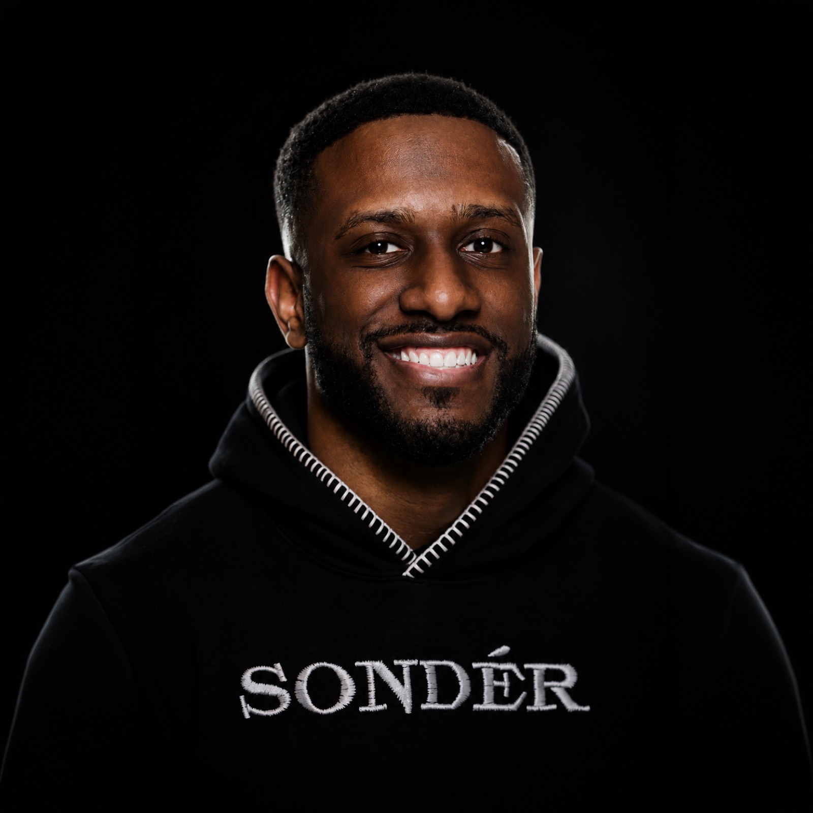 David Balan smiling, in a black hoodie against a dark background