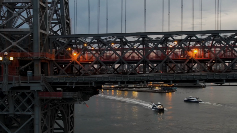 A ferry passing under the bridge at dusk, its wake trailing across the river